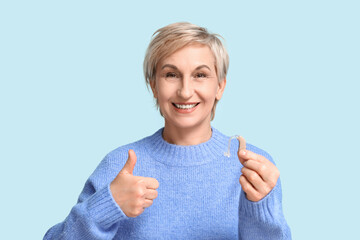 Poster - Mature woman with hearing aid showing thumb-up gesture on blue background