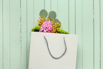 Wall Mural - Paper shopping bag with flowers and eucalyptus on green wooden background
