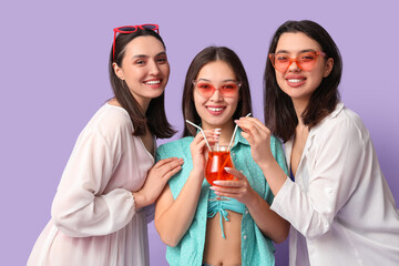 Wall Mural - Beautiful young women with glass of cocktail on lilac background. Summer party