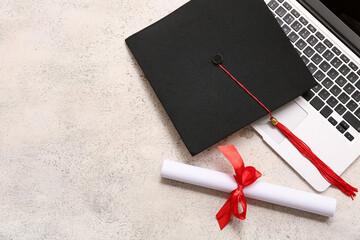 Diploma with red ribbon, modern laptop and graduation hat on white grunge background