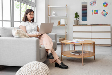 Sticker - Young interior designer working with laptop on sofa in office