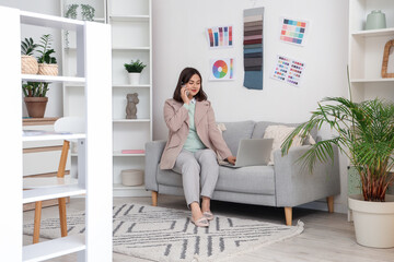 Poster - Beautiful interior designer with laptop talking by mobile phone on sofa in office