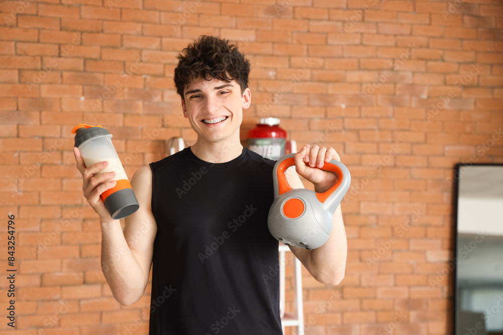 Sporty young man with protein shake and kettlebell in gym