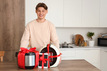 Poster - Young man with gift multicooker and coffee machine on table in kitchen