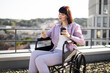 © sofiko14 - Woman in wheelchair holding cup of coffee and smartphone while enjoying view from rooftop. Depicts independence, modern lifestyle, and city life.