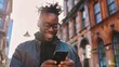 © MD Media - Photo of a happy man looking at his phone on the street in an urban setting. He is smiling and wearing modern clothing. The background features buildings