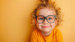 © KEA - Happy and playful little curly blond girl with big eyeglasses on yellow background