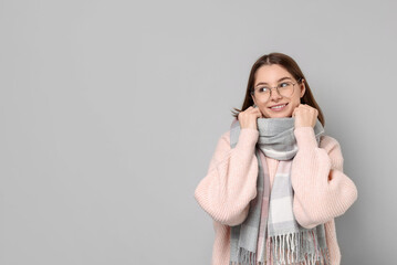 Wall Mural - Beautiful woman in warm scarf and glasses on gray background, space for text