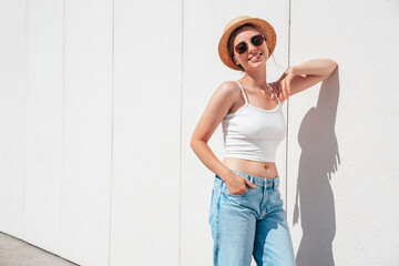 Beautiful smiling model in sunglasses. Female dressed in summer hipster white T-shirt and jeans. Posing  wall in the street. Funny and positive woman having fun outdoors, in hat, sunglasses