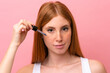 © luismolinero - Young redhead woman isolated on pink background holding a serum. Close up portrait