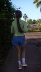 Wall Mural - Woman with long hair jogging in park, listening to music on headphones in morning sun