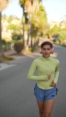 Wall Mural - A woman jogging outdoors with headphones on a sunny day along a treelined path