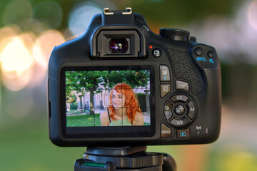 Camera taking a photo of a red haired model woman outdoors. Photography concept