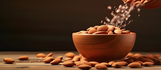 Poster - Almond is poured into a wooden bowl Brown background with copy space