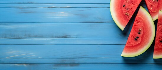 Wall Mural - Copy space image of a sliced watermelon placed on a blue wooden background presented in a flat lay composition with a top view perspective