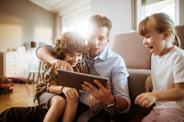 Wall Mural - Happy father using tablet with two children enjoying family time at home