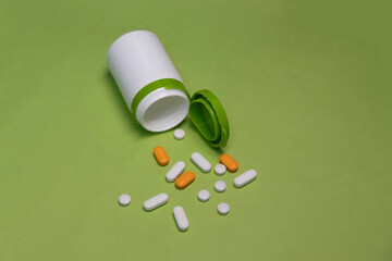 Pills pouring out of medicine bottle on green background