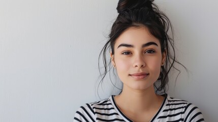 Canvas Print - Shy and positive girl in striped shirt looking attentively at the camera while standing on a white backdrop