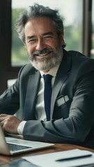 Wall Mural - Man in suit is smiling and sitting at desk with laptop