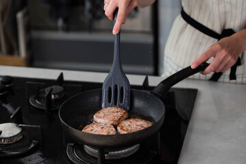 Meatballs or small meat patties cutlets sizzling in oil while frying in a pan on the stove. Concept of home cooking, traditional recipes, and culinary preparation