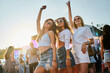 © artiemedvedev - Group of diverse girls having fun at coastal music festival. Women dance, smile in sunlight by sea. Friends enjoy live band, sunset party vibes on sandy beach. Youth culture, summer event gathering.