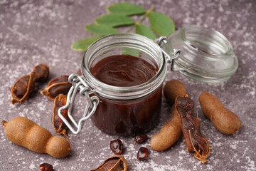 Wall Mural - Jar with tasty tamarind jam and fruits on grey background