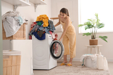 Wall Mural - Young woman putting dirty laundry into washing machine at home