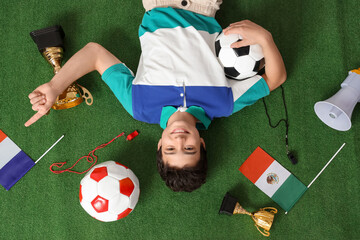 Wall Mural - Teenage boy with soccer balls, flags and gold cups lying on green grass