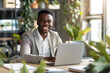 © lashkhidzetim - Black man in a suit is smiling and sitting at a table with a laptop. He is happy and content while working on his computer