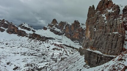 Wall Mural - Aerial around view of amazing rocky mountains in snow under moody gray clouds, Dolomites, Italy, 4k