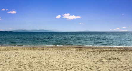 Wall Mural - Greek empty sandy beach. Ripple sea water, blue sky background, copy space. Summer holiday template