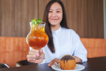 Wall Mural - Portrait image of a woman holding a glass of iced lemon tea with chocolate Timber Ring Croissant on the table