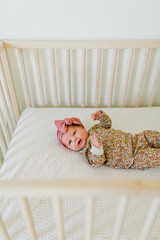 Wall Mural - Newborn baby girl lays in floral onesie in wooden crib