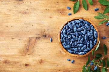 Wall Mural - Wooden bowl with fresh honeysuckle berry on table top view. Organic superfood and healthy berry.