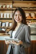 © pham - A young woman in a gray blazer smiles while holding a tablet in a modern coffee shop