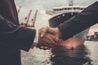 © DK_2020 - A businessman shaking hands with a logistics partner in front of a streamlined modern cargo ship representing successful negotiations