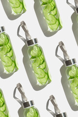 Wall Mural - Glass bottles with cucumber water drink detox at sunlight on white background, repeated pattern. Healthy infused water boost metabolism, weight loss. Aesthetic still life, refreshing drink