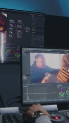 Fototapete - African American movie maker does color grading on computer in studio with equipment. Big monitors with action film footage and professional software interface on wall. Video post production process.