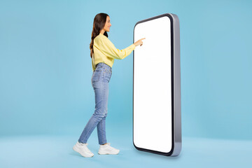 Woman standing in front of huge smartphone, touching mobile phone empty display and smiling, using newest mobile app, blue background, copy space