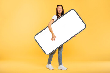 Great application. Happy young European lady holding huge smartphone with blank screen, woman advertising new mobile app or website, mockup