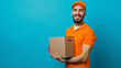 © Natali - Half-body HDR image of a smiling courier in orange uniform carrying a cardboard box against a bright blue background, isolated on the right. Depicts efficient delivery services and customer