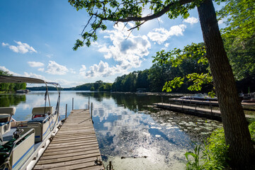 Looking out onto a Wisconsin lake in the late afternoon on a calm day from the shore with a  pontoon boat  by the side of a pier.