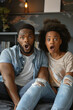 © Fabio - Diverse couple watching TV at home, showing surprise
