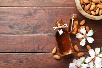 Wall Mural - Almond oil in bottles, flowers and bowl with nuts on wooden table, flat lay. Space for text