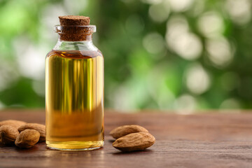Wall Mural - Almond oil in bottle and nuts on wooden table against blurred green background, closeup. Space for text