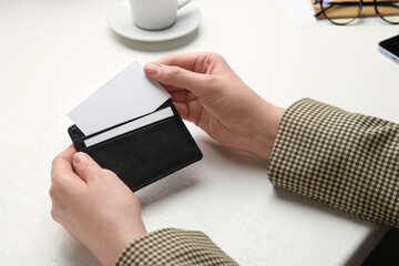 Wall Mural - Woman holding leather business card holder with blank card at white table, closeup