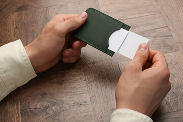 Wall Mural - Man holding leather business card holder with cards at wooden table, closeup