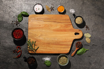Wall Mural - Wooden cutting board surrounded by spices on gray textured table, flat lay. Space for text