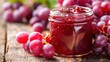 © weerasak - Close-up of a glass jar filled with delicious grape jam surrounded by fresh ripe grapes on a wooden table, showcasing fresh and sweet flavors.