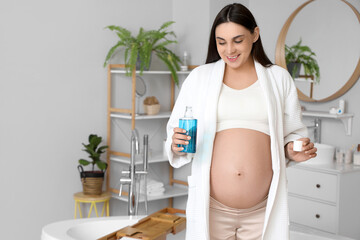 Wall Mural - Young pregnant woman with mouth rinse in bathroom